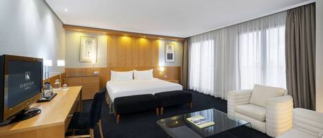 A hotel room with a bed, a desk with a computer, a sofa, and a coffee table.