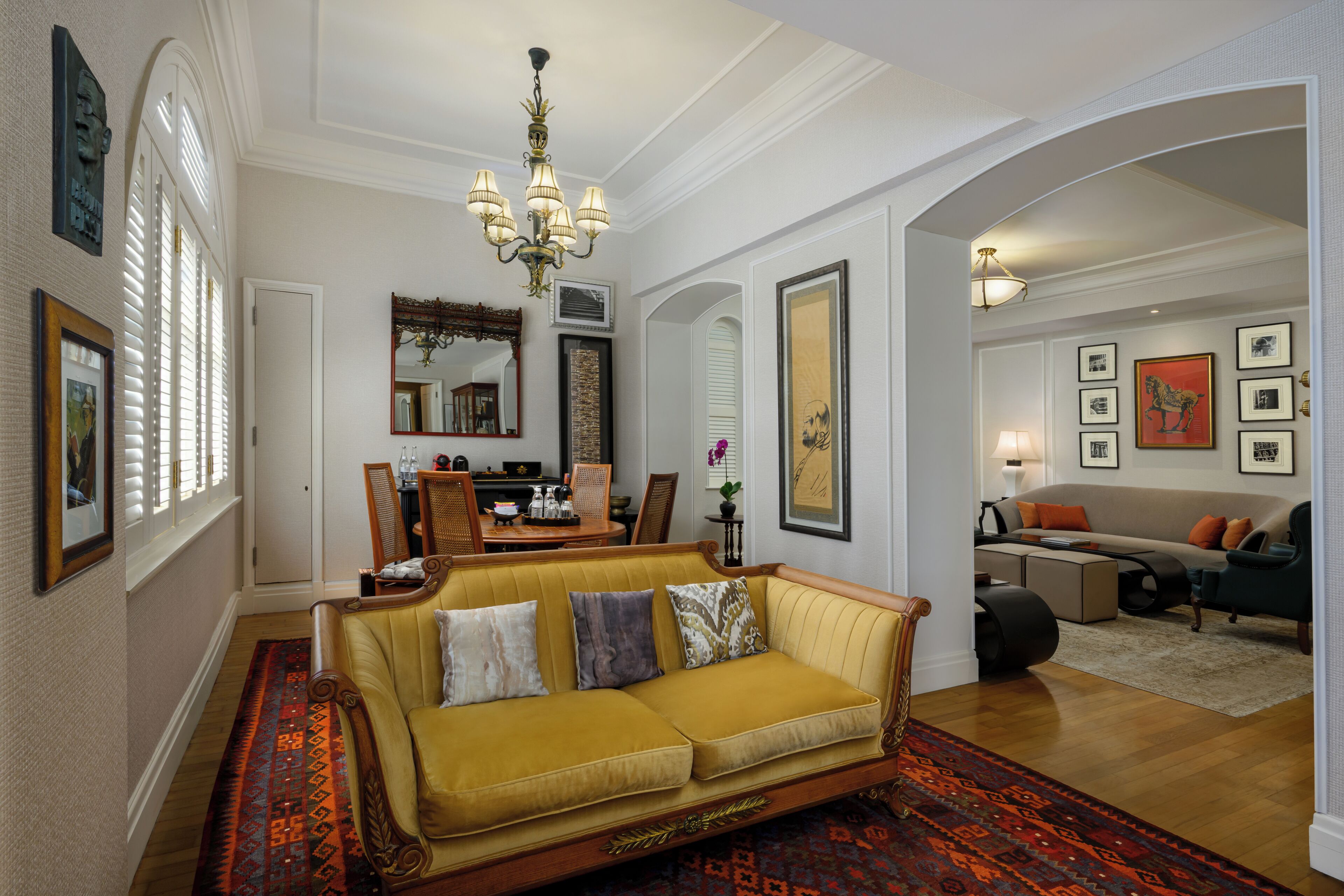 A spacious living room with a yellow sofa, a chandelier, and a dining area with a table and chairs.