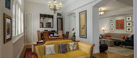 Un salón espacioso con un sofá amarillo, una araña y un comedor con mesa y sillas.