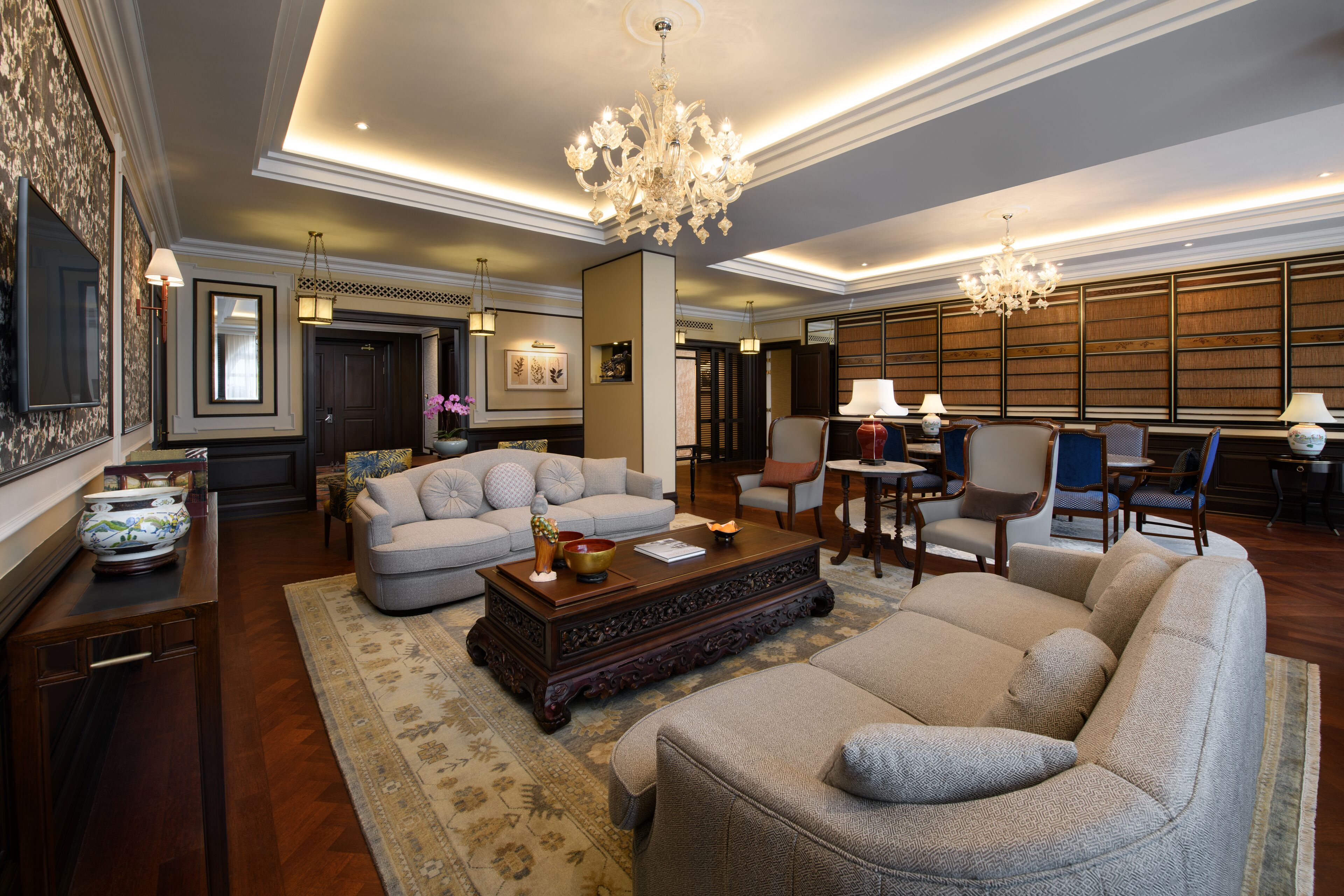 A spacious living room with a large sectional sofa, a wooden coffee table, and a chandelier. There is a dining area with a table and chairs in the background.
