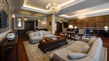 A spacious living room with a large sectional sofa, a wooden coffee table, and a chandelier. There is a dining area with a table and chairs in the background.