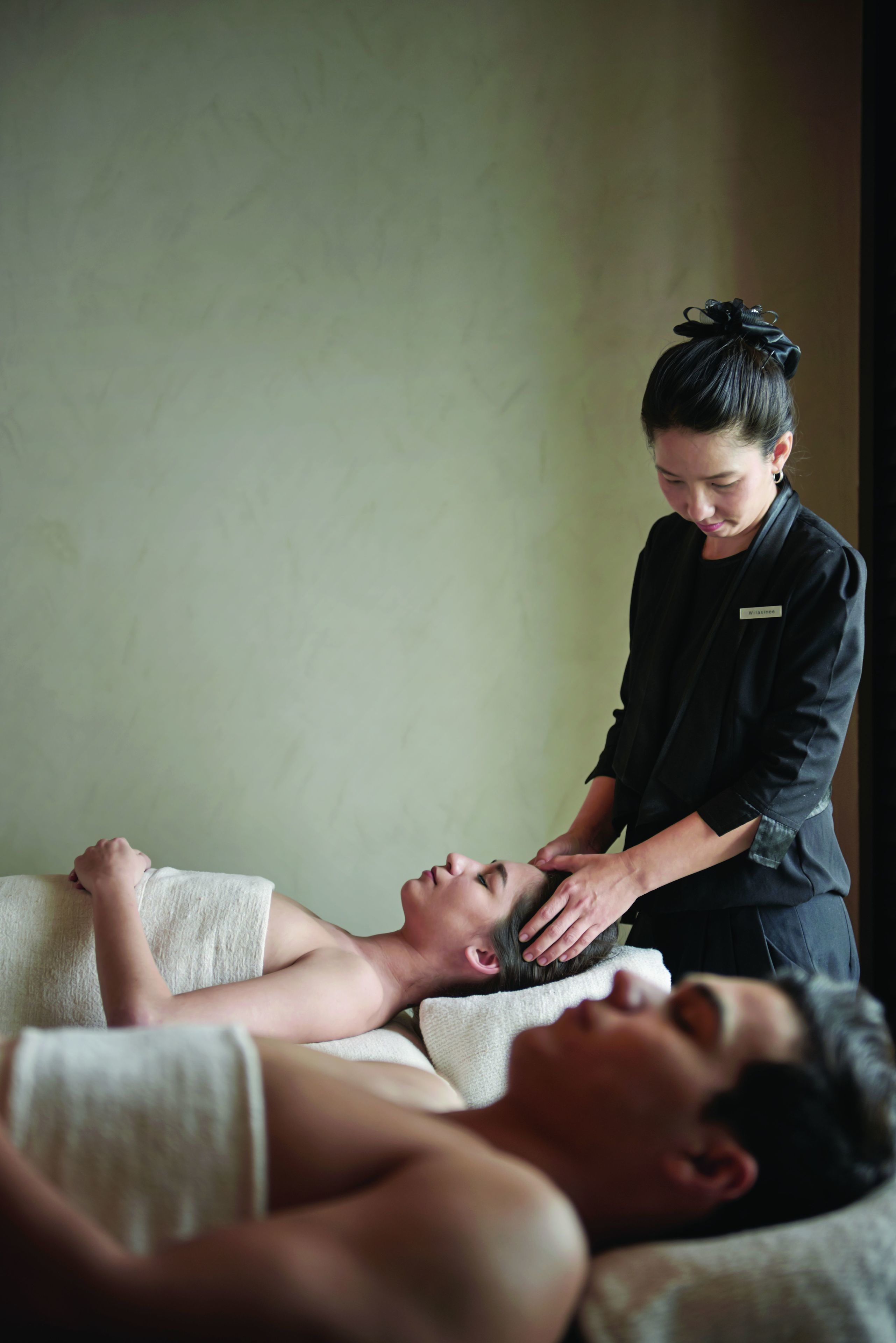 A person receiving a massage in a room with a plain wall and a single bed.
