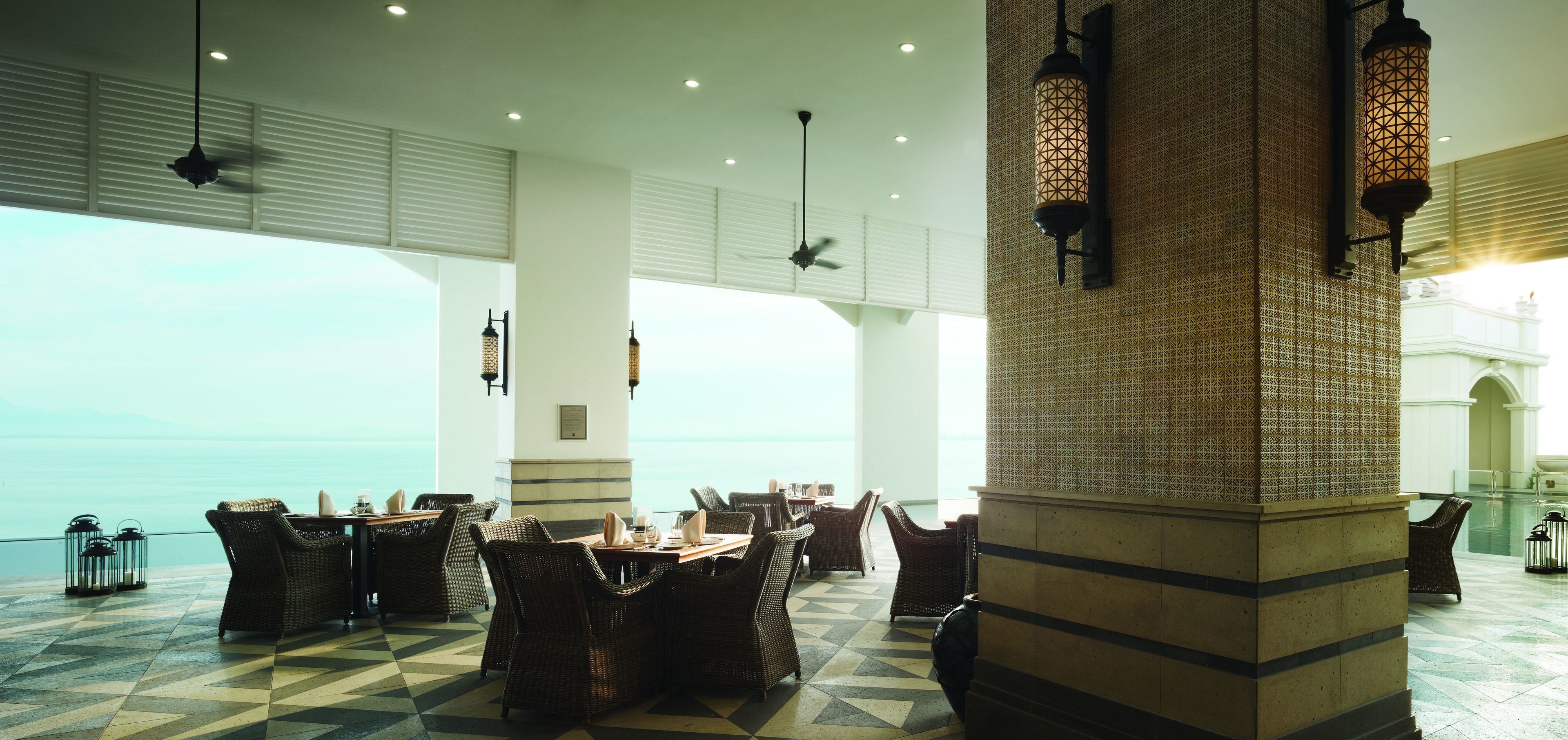 Un comedor espacioso con mobiliario de mimbre, un pilar decorado y vistas al mar.
