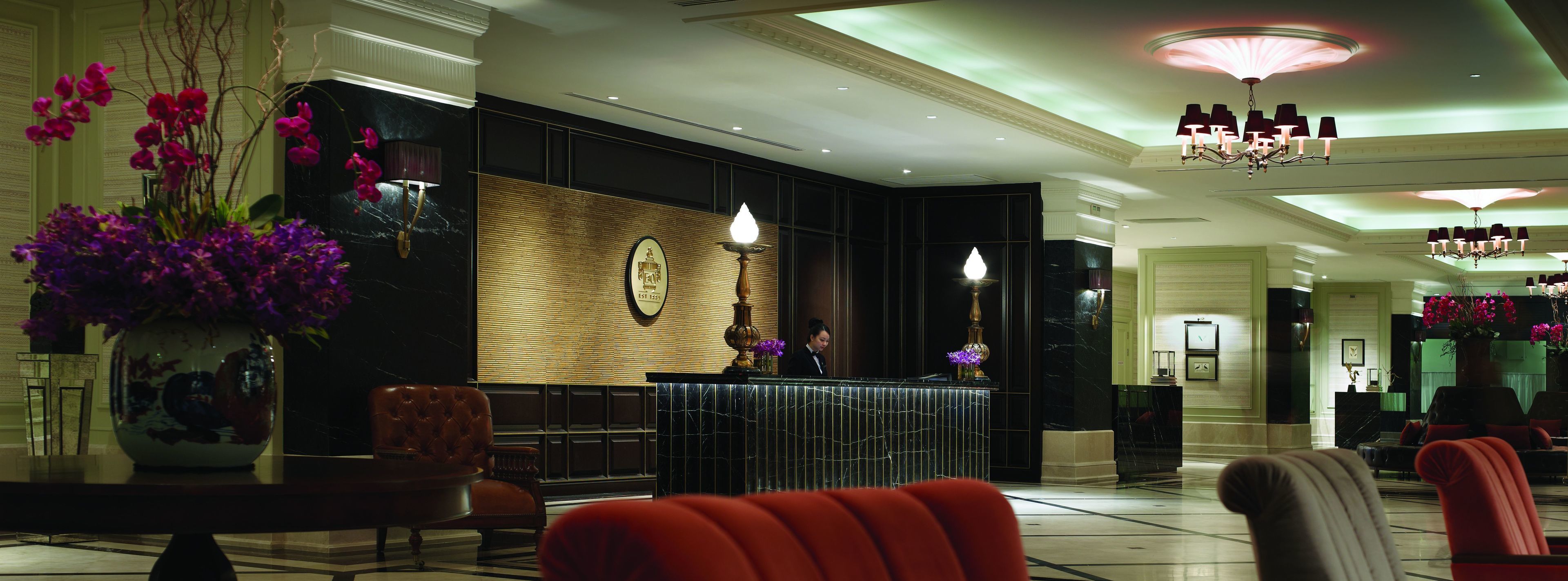 A hotel lobby with a reception desk, seating area, and decorative elements like vases and chandeliers.