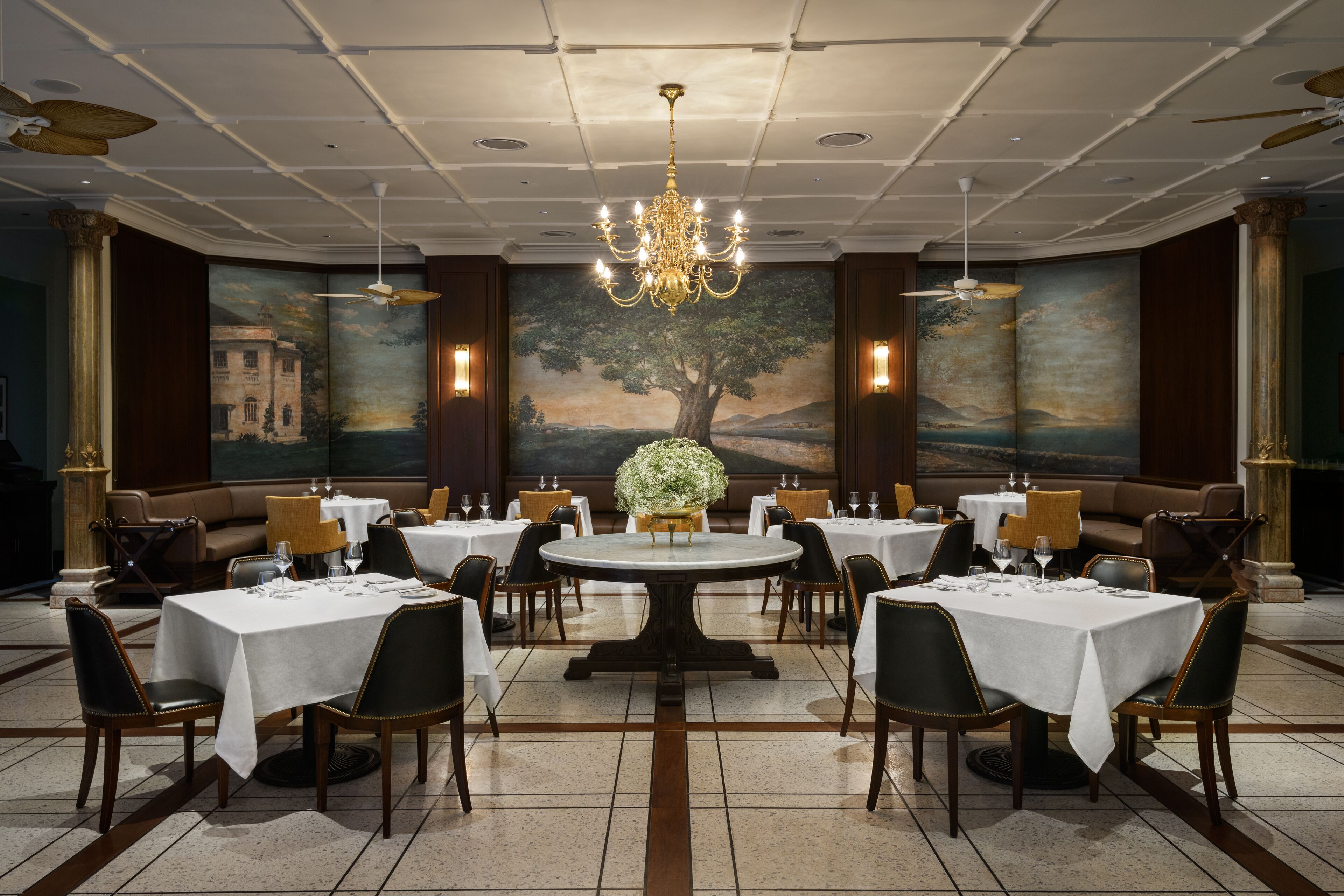 A formal dining room with round tables, black chairs, and a chandelier.
