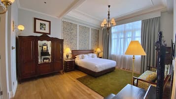 A hotel room with a large bed, a wooden wardrobe, a desk, and a chandelier.