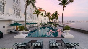 A heritage wing swimming pool with lounge chairs, palm trees, and a view of the city skyline. - Eastern And Oriental Hotel (George Town)