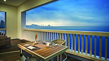A balcony with a table set for dining, overlooking a city skyline and the ocean.