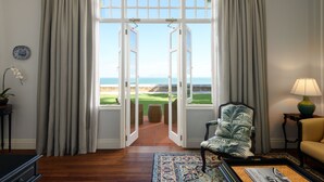 A room with a view of the ocean, a chair, a lamp, and a rug. - Eastern And Oriental Hotel (George Town)