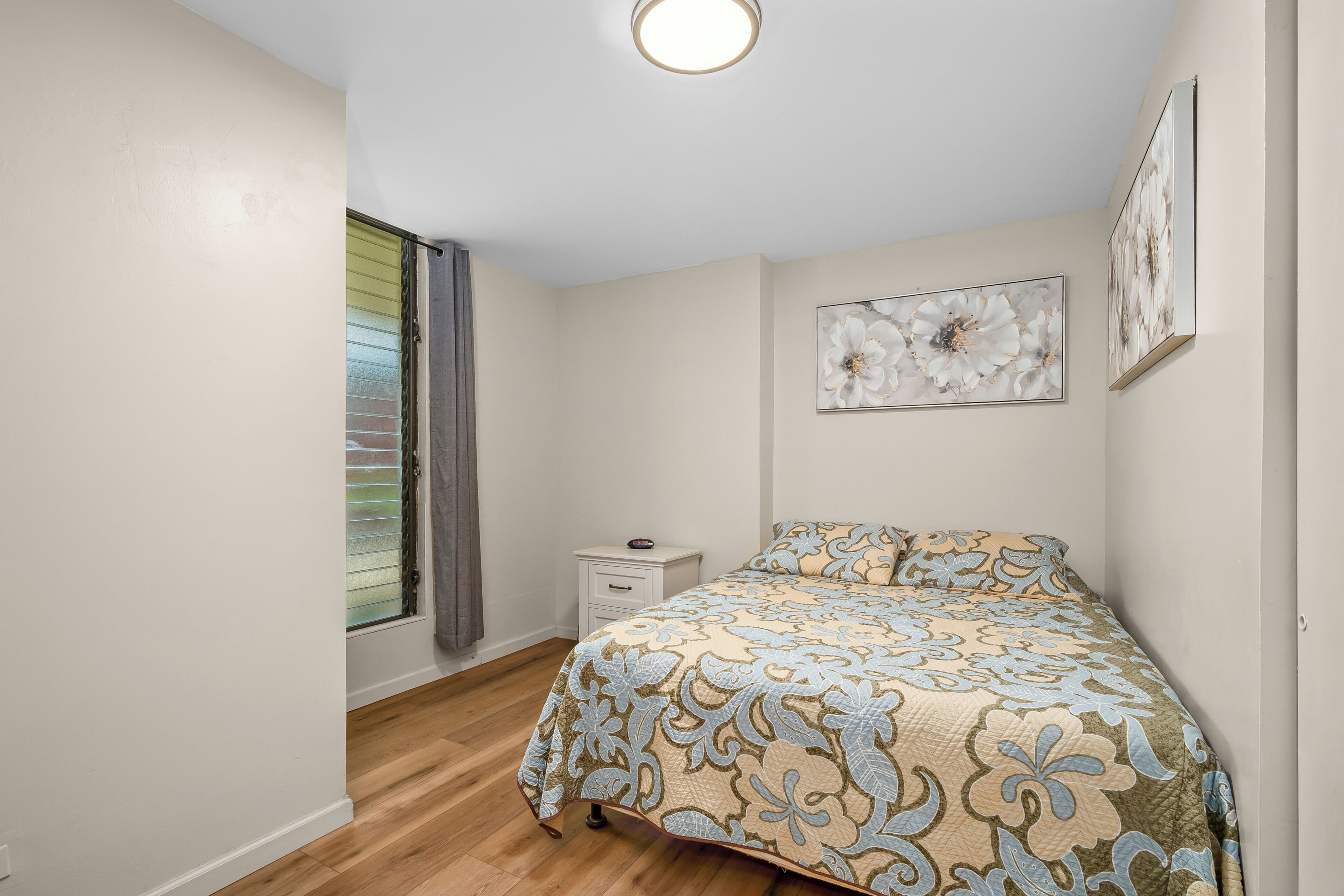 A bedroom with a bed, a nightstand, a window with blinds, and wall art.