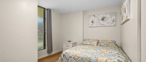 A bedroom with a bed, a nightstand, a window with blinds, and wall art.