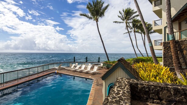 A pool area with lounge chairs and a view of the ocean.