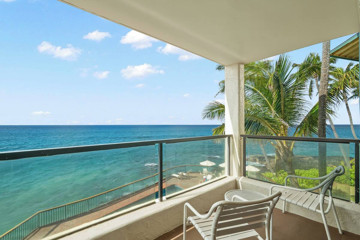 A balcony with a view of the ocean, a table, and a chair.