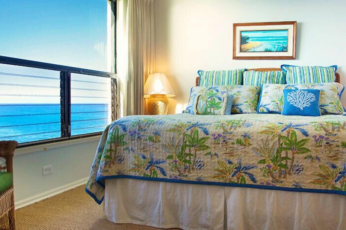 A bedroom with a large bed, a view of the ocean, and a framed picture on the wall.