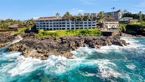 A coastal hotel with multiple balconies, a rocky shoreline, and palm trees.