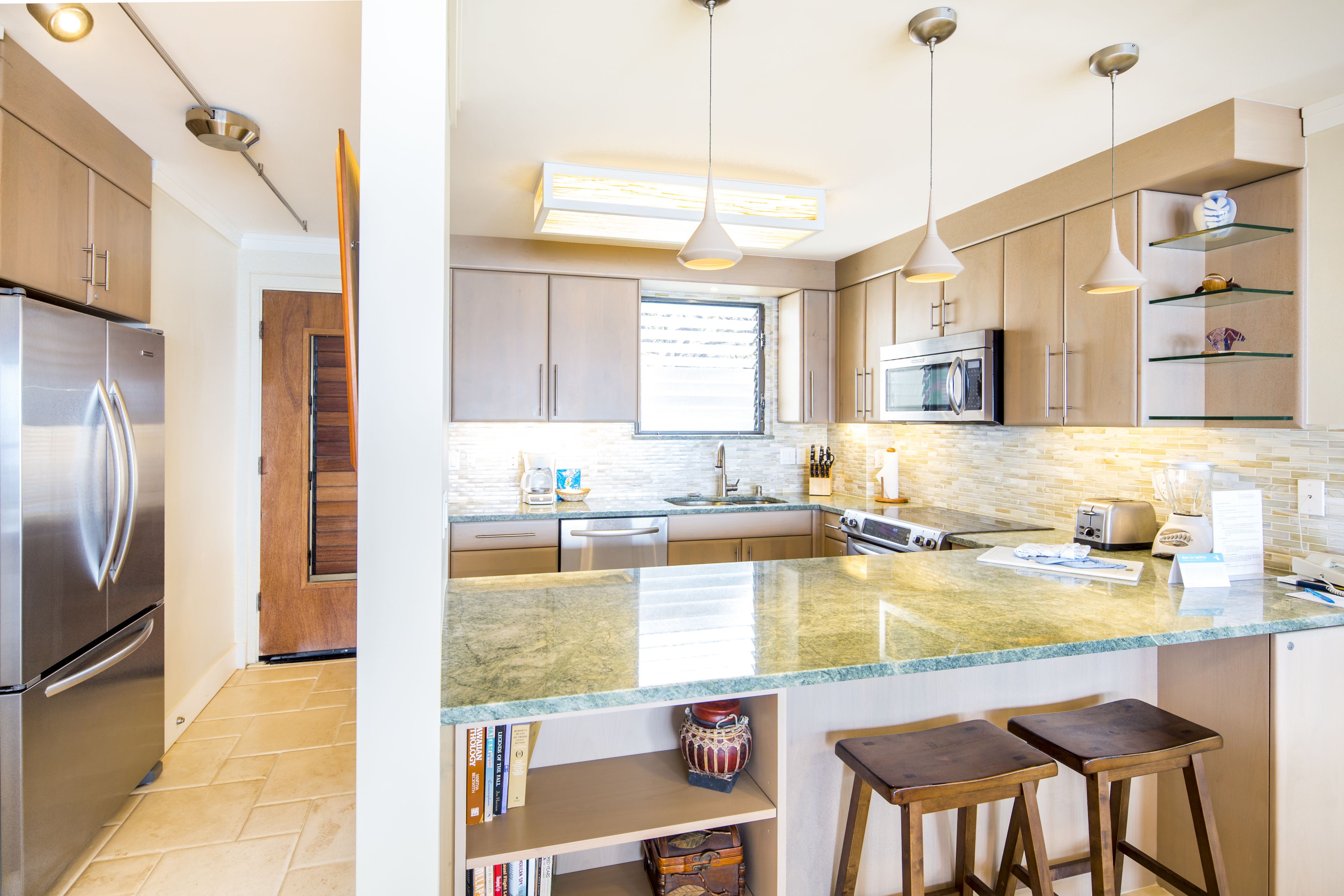 A modern kitchen with stainless steel appliances, a large island with stools, and pendant lighting.