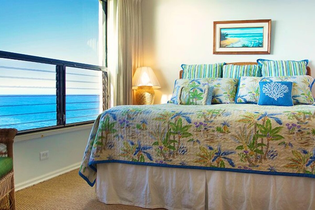 A bedroom with a large bed, a view of the ocean, and a framed picture on the wall.