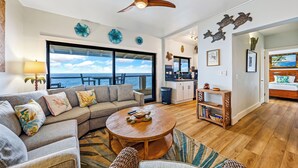 A spacious living area with a large window overlooking the ocean, a ceiling fan, and a cozy seating arrangement.