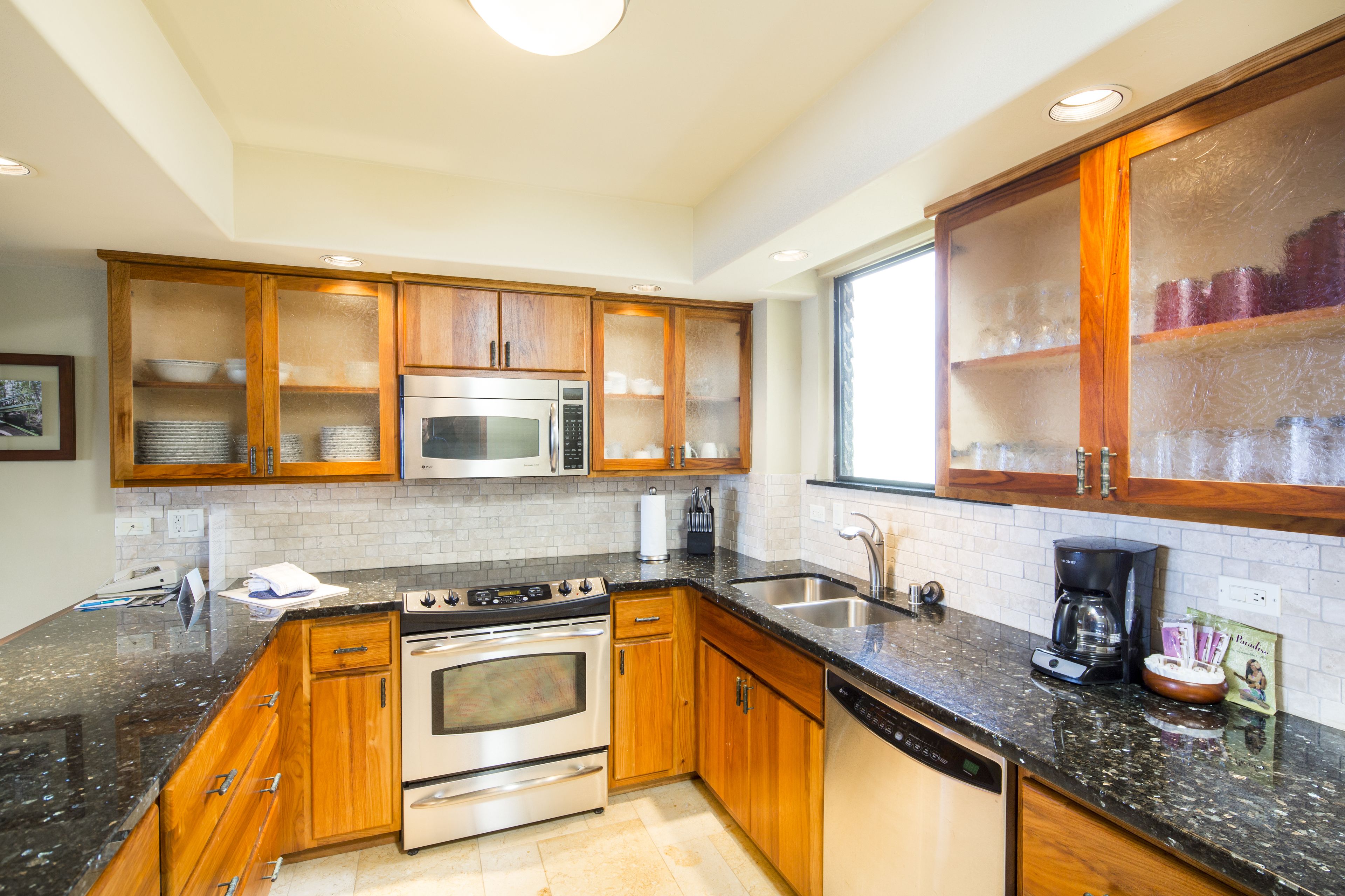 A kitchen with wooden cabinets, stainless steel appliances, a granite countertop, and a window providing natural light.