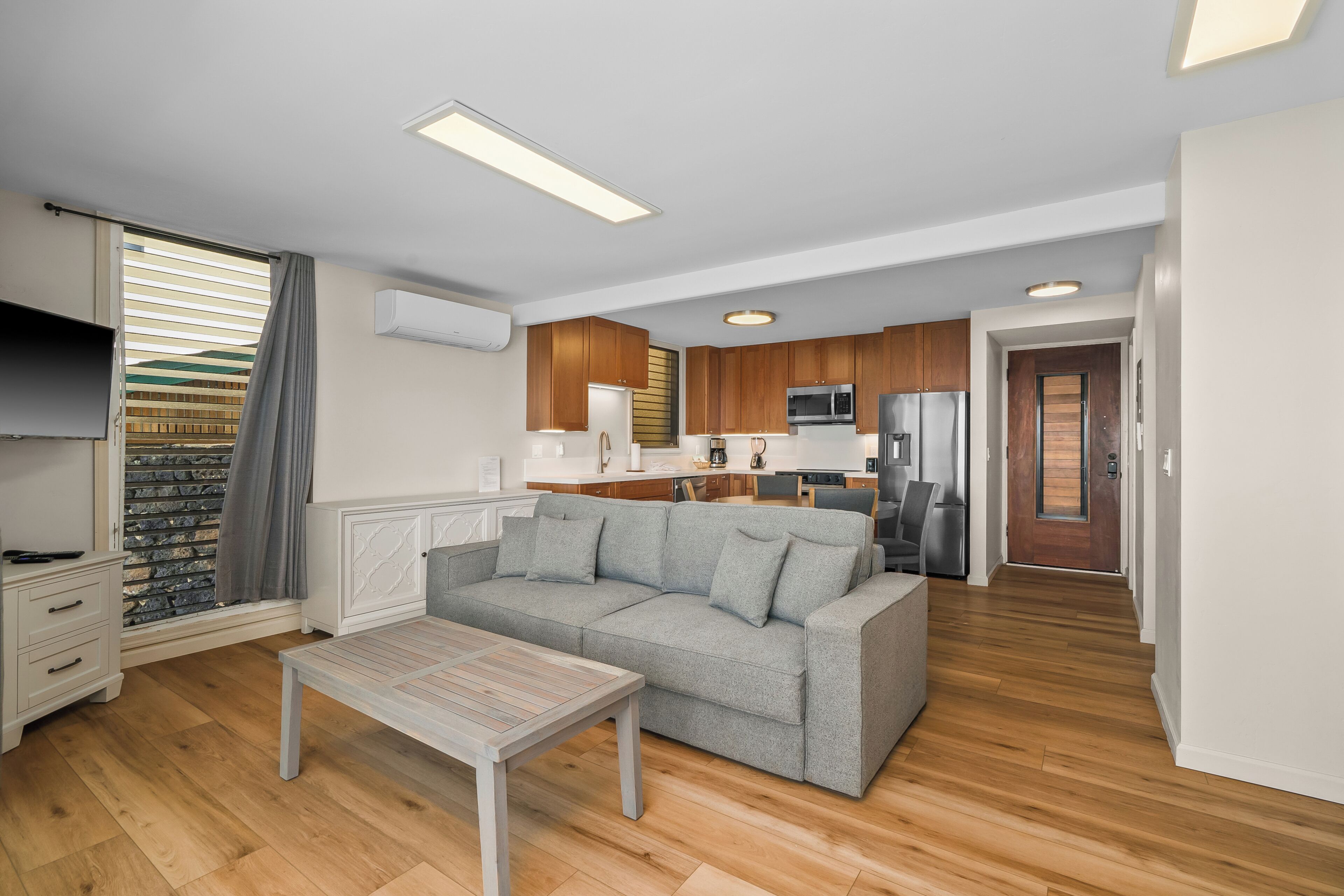 Una sala moderna con un sofá gris, una mesa de centro de madera y una cocina al fondo.