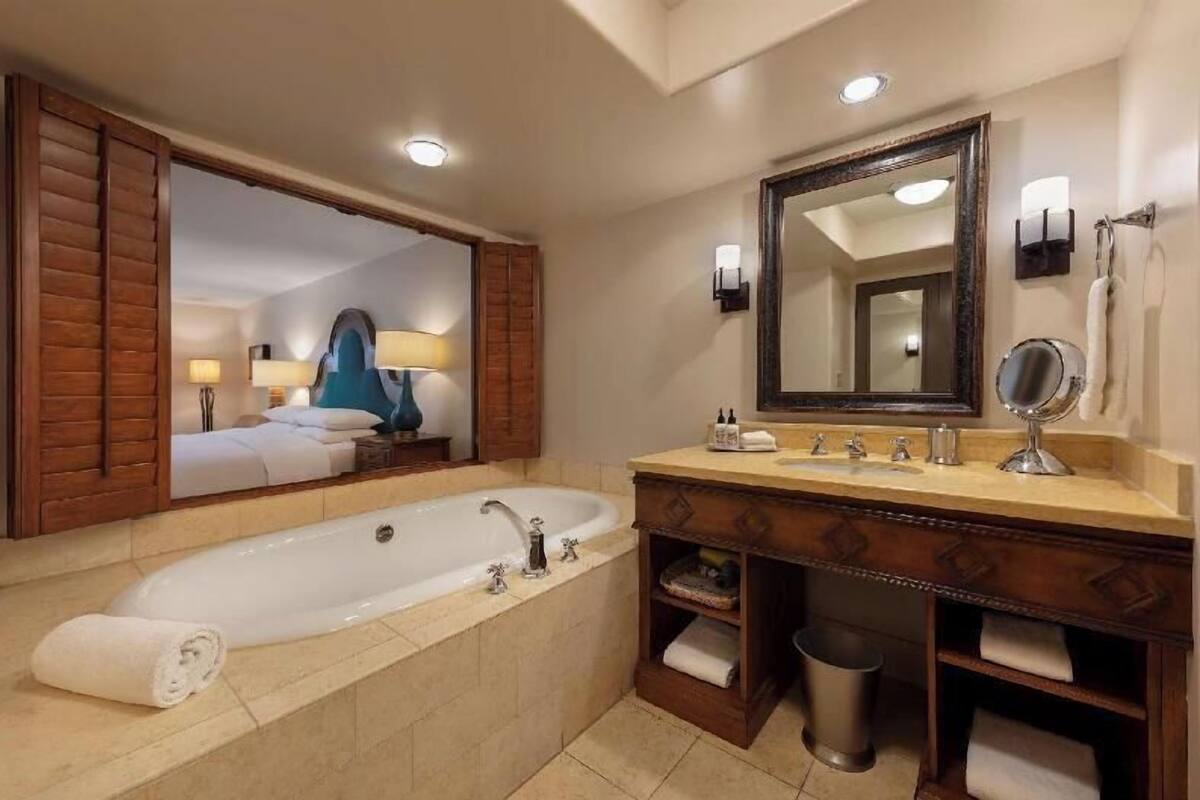 Ein Badezimmer mit einer großen Badewanne, einem Waschtisch inklusive Spiegel und einem Handtuchhalter.