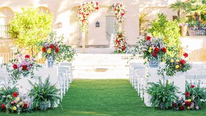 An outdoor wedding venue with white chairs arranged in rows, a central aisle, and floral decorations.