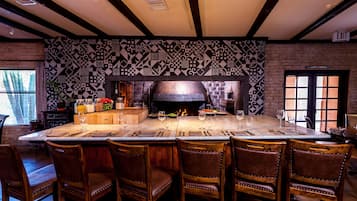 Un restaurante con una mesa común alargada, sillas de madera y un muro con estampado.