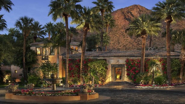 A hotel with a courtyard, palm trees, and a mountain backdrop.
