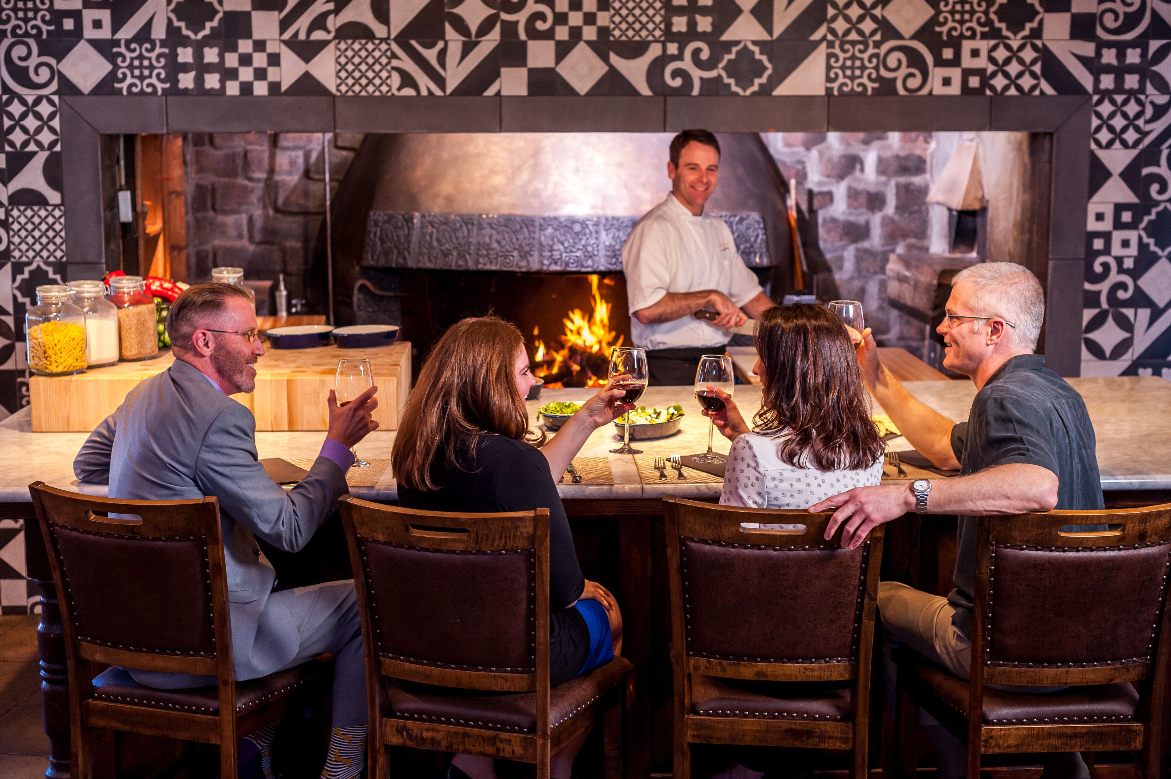 Un groupe de personnes est réuni dans un restaurant qui possède une cheminée en pierre et des murs recouverts de carreaux décoratifs.