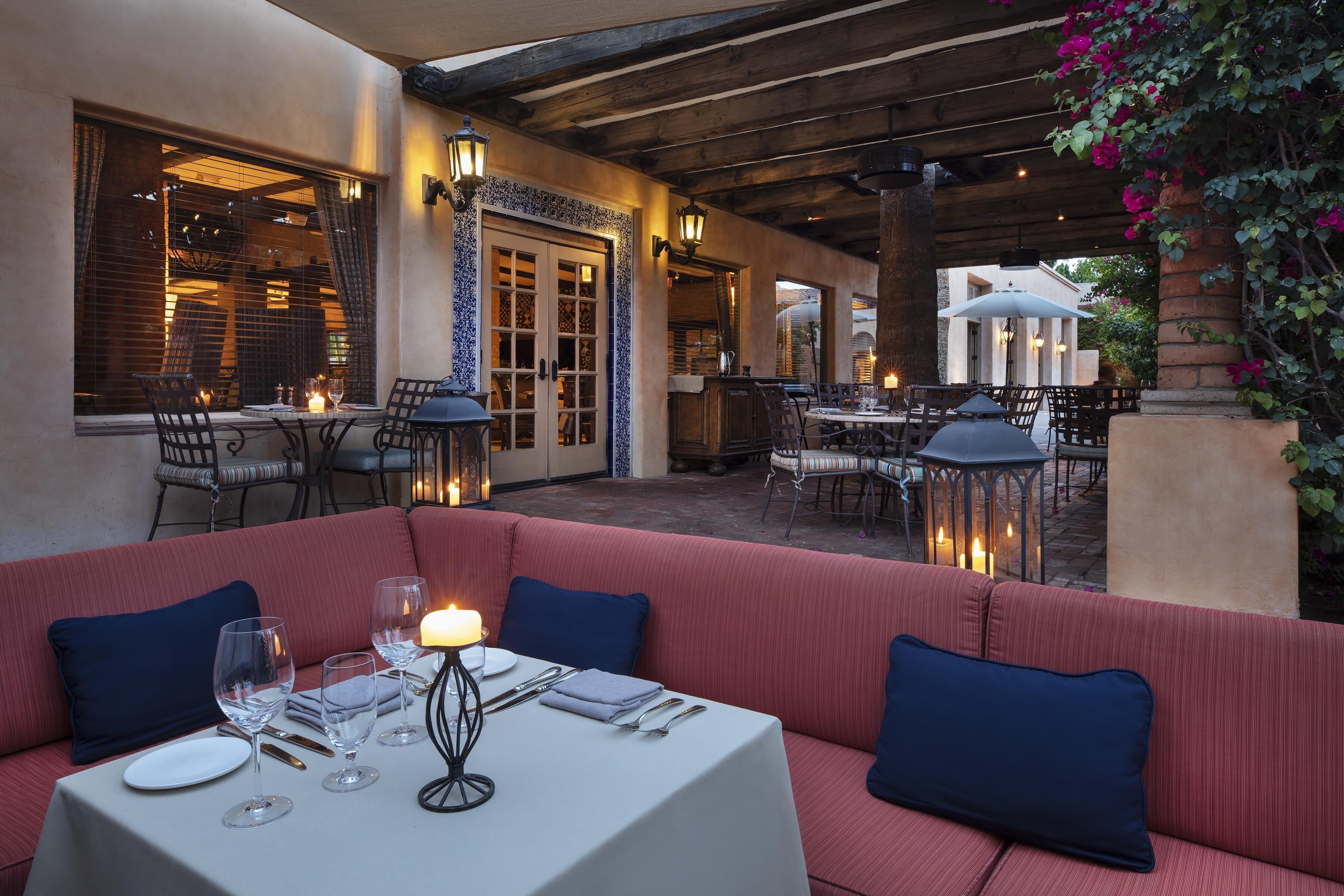 An outdoor dining area with a red cushioned bench, white tablecloth, and candle centerpiece.