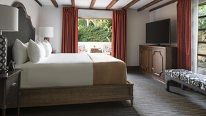 A hotel room with a large bed, a television, a bench, and a view of the outdoors.