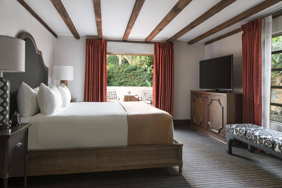 Ein Hotelzimmer mit einem großen Bett, einem Fernseher, einer Sitzbank und Blick ins Freie.
