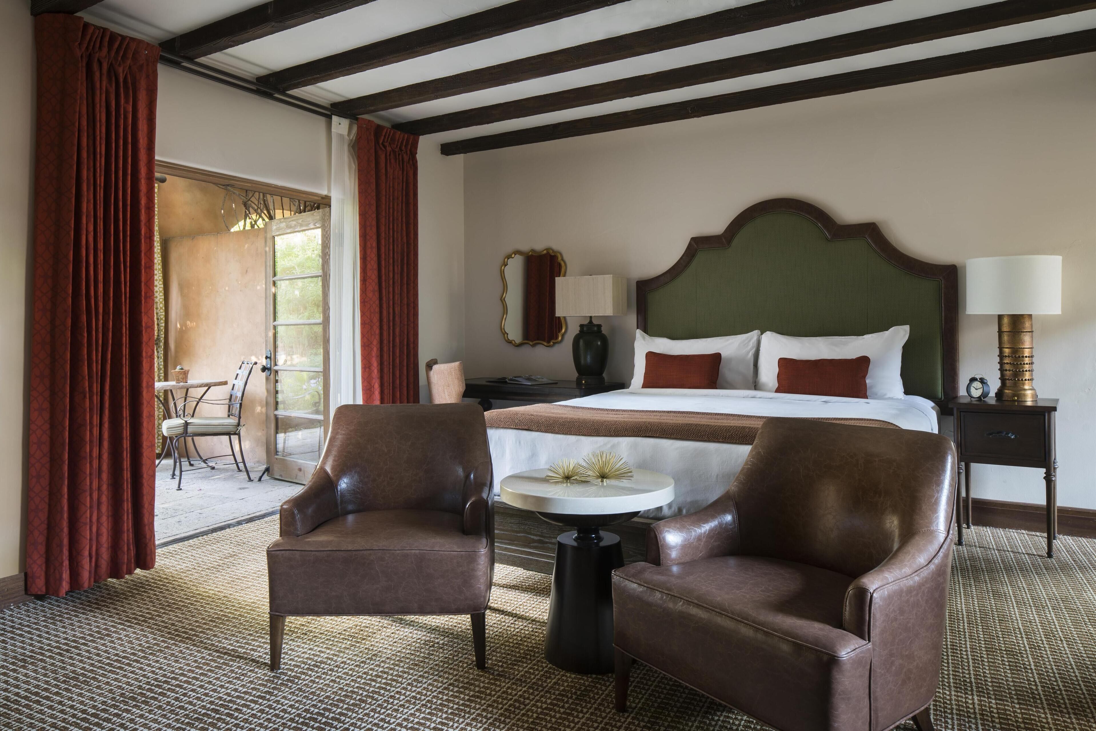 Una camera d'albergo con un letto, due poltrone in pelle, un piccolo tavolo rotondo e un comodino con una lampada.