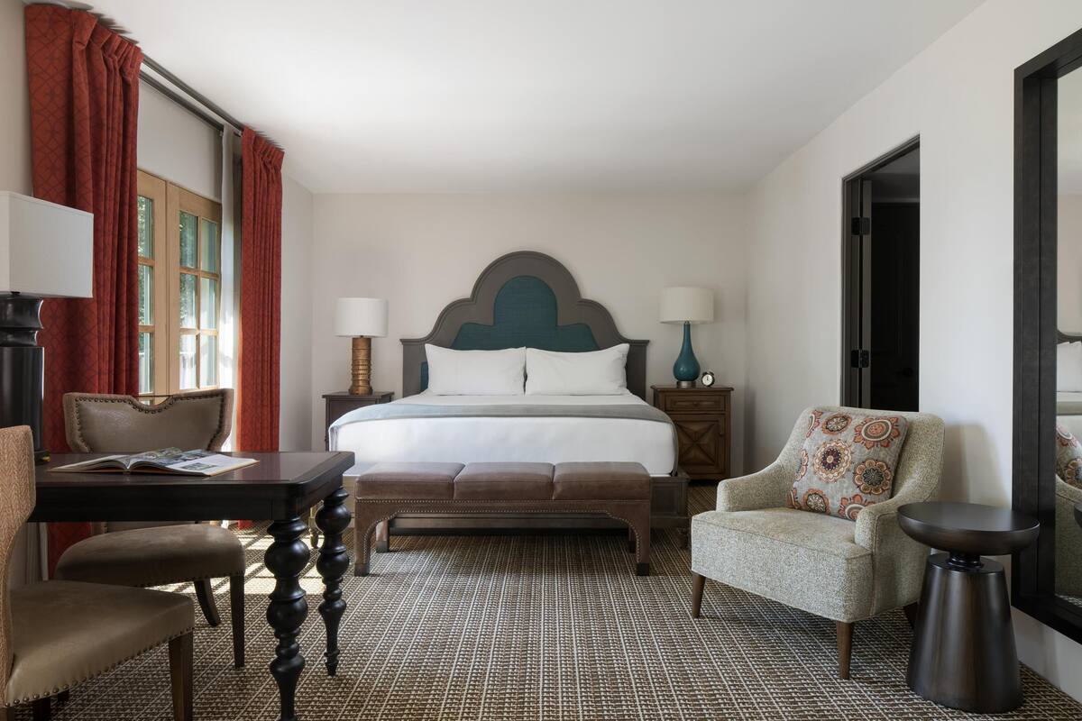 Ein Hotelzimmer mit einem großen Bett, einem Schreibtisch mit Stuhl, einem Nachttisch und einem gestreiften Boden.