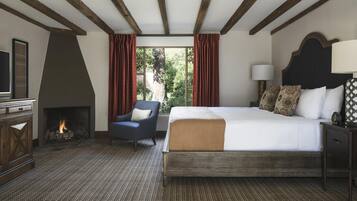 Une chambre d’hôtel avec une cheminée, un lit agrémenté d’oreillers à motifs, une table de chevet avec une lampe, et une vue sur la verdure à l’extérieur.