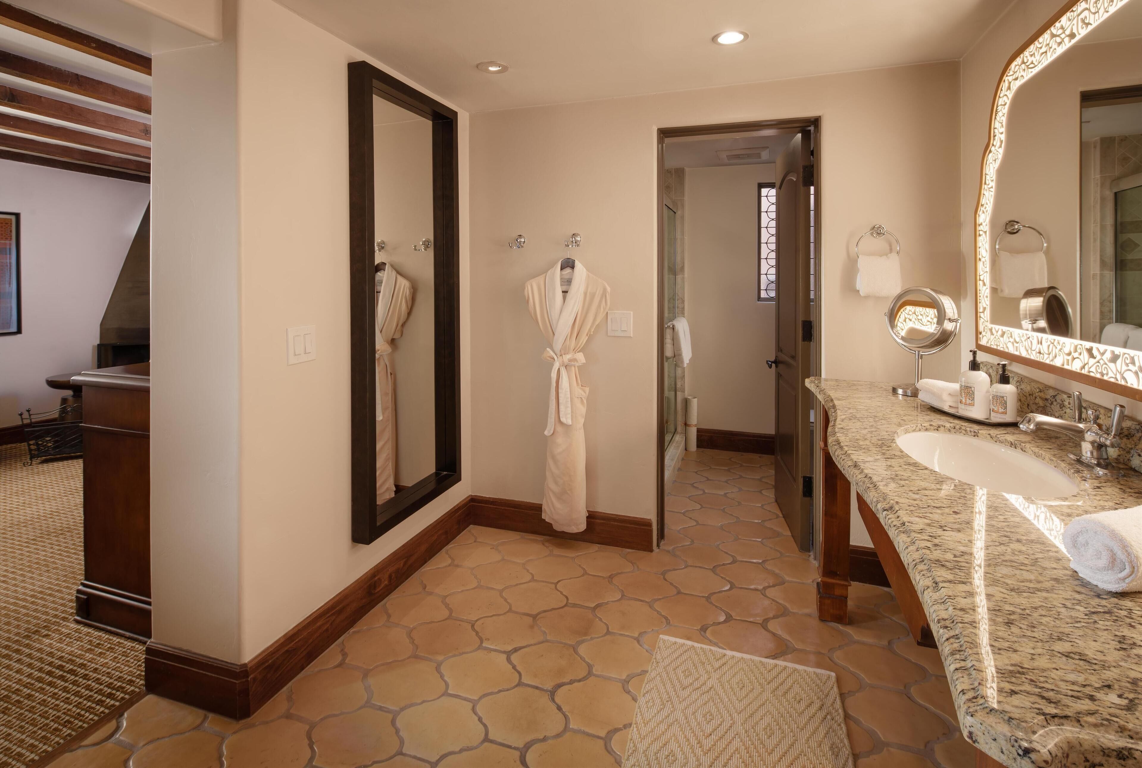 A modern bathroom with a large mirror, a sink, and a robe hanging on the wall.