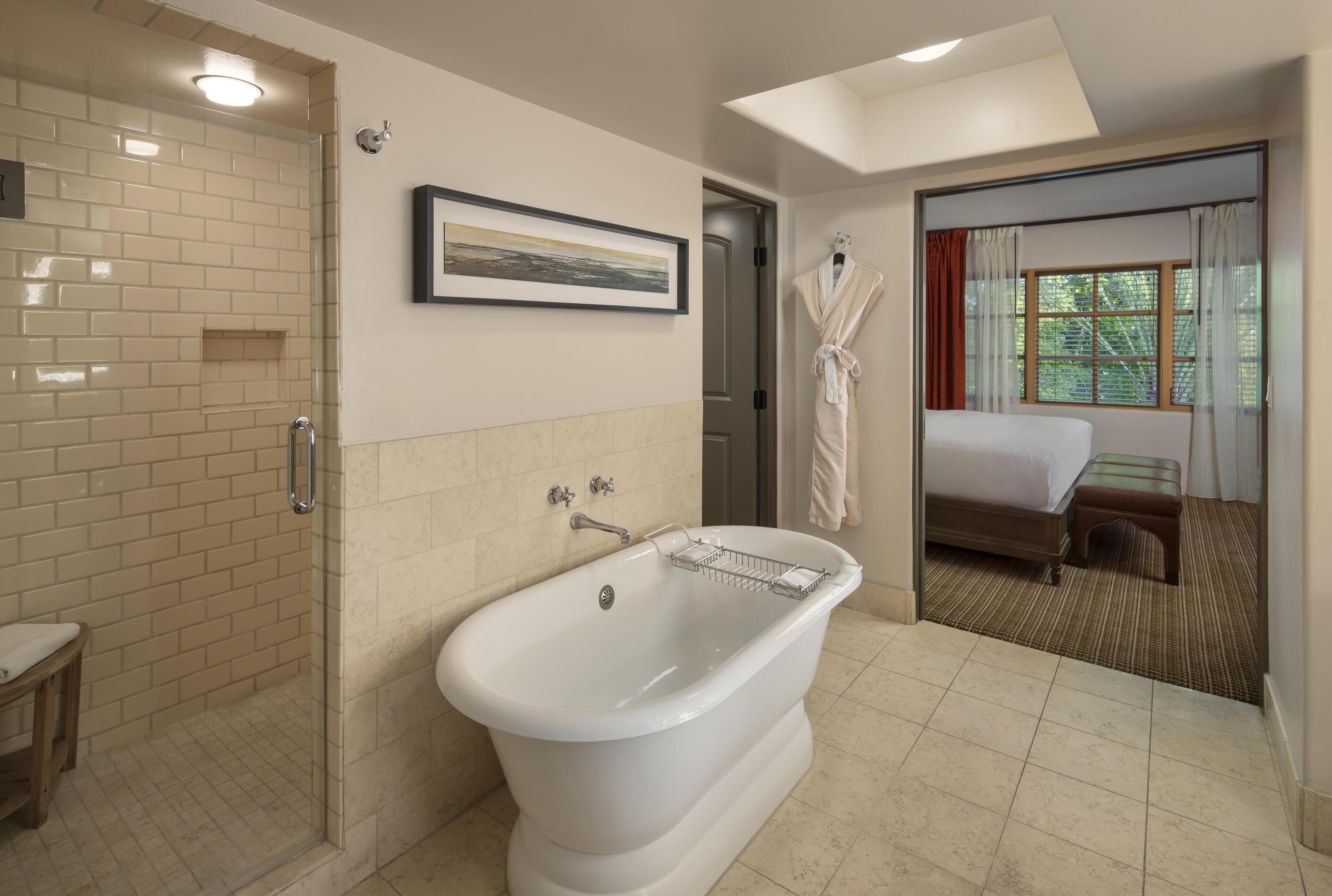 A bathroom with a bathtub, a shower, and a bed visible through an open door.