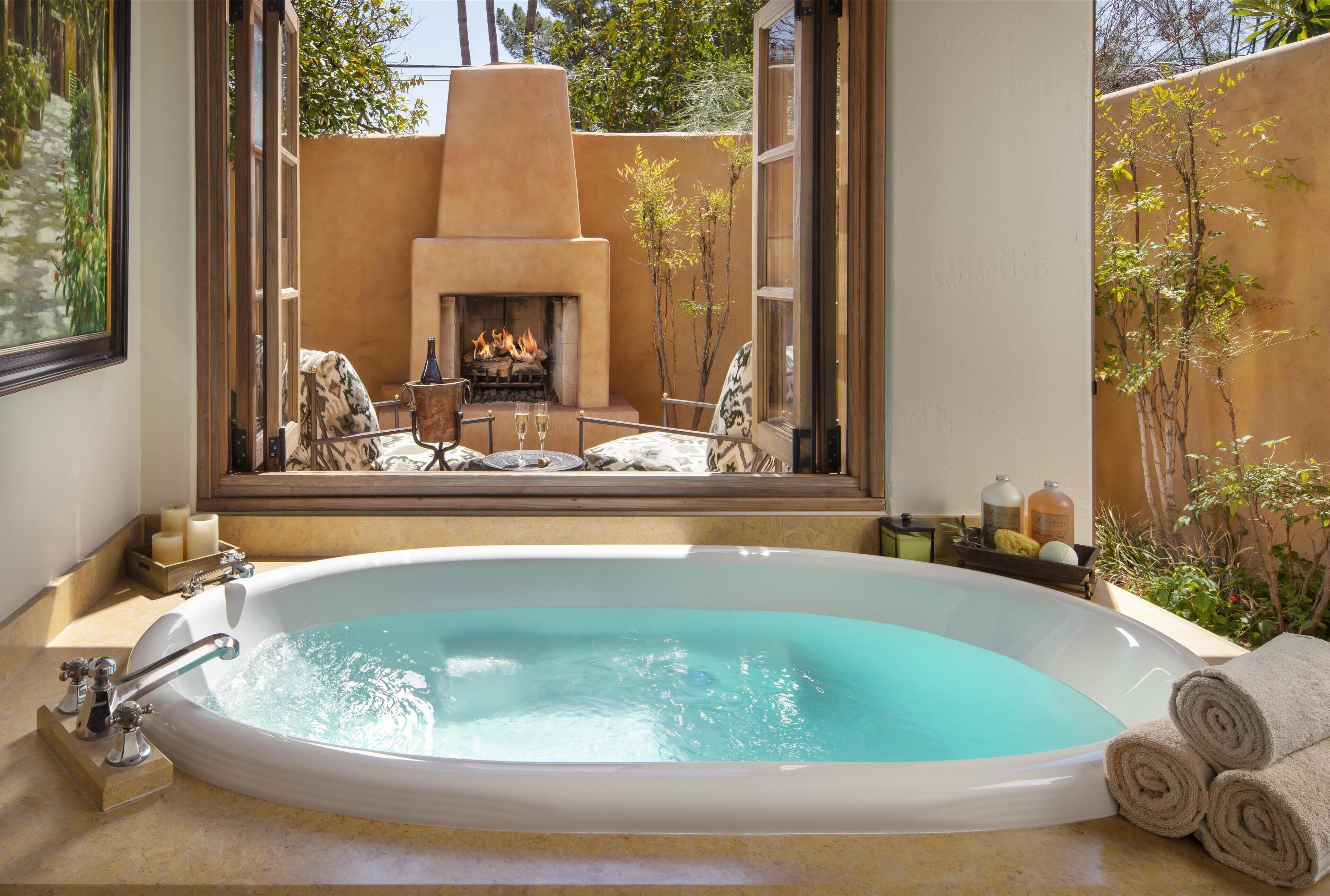 A large oval bathtub with a view of an outdoor patio and a fireplace.