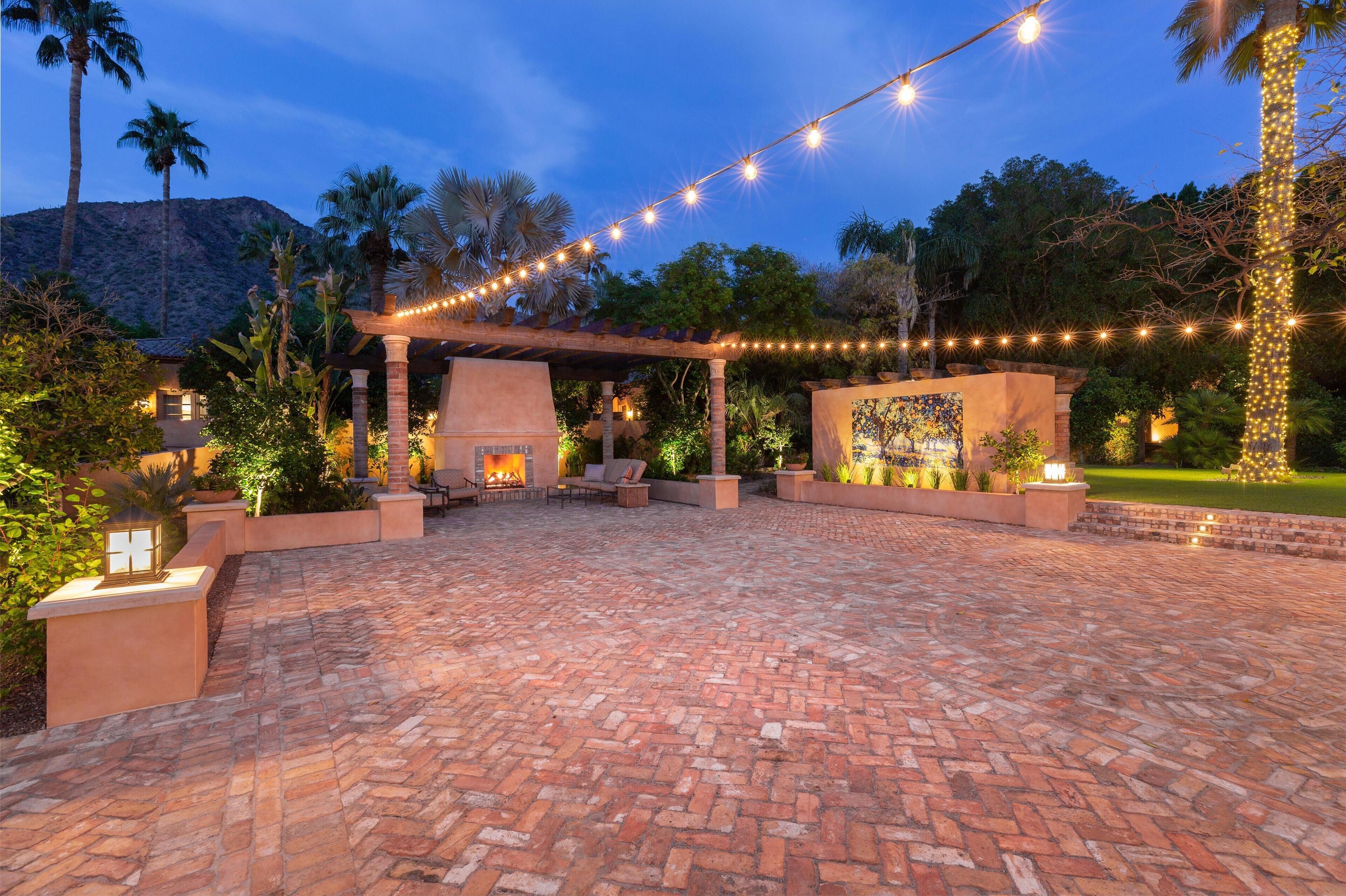 An outdoor patio with a brick floor, string lights, and a fire feature.