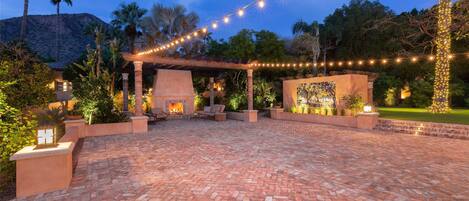 An outdoor patio with a brick floor, string lights, and a fire feature.