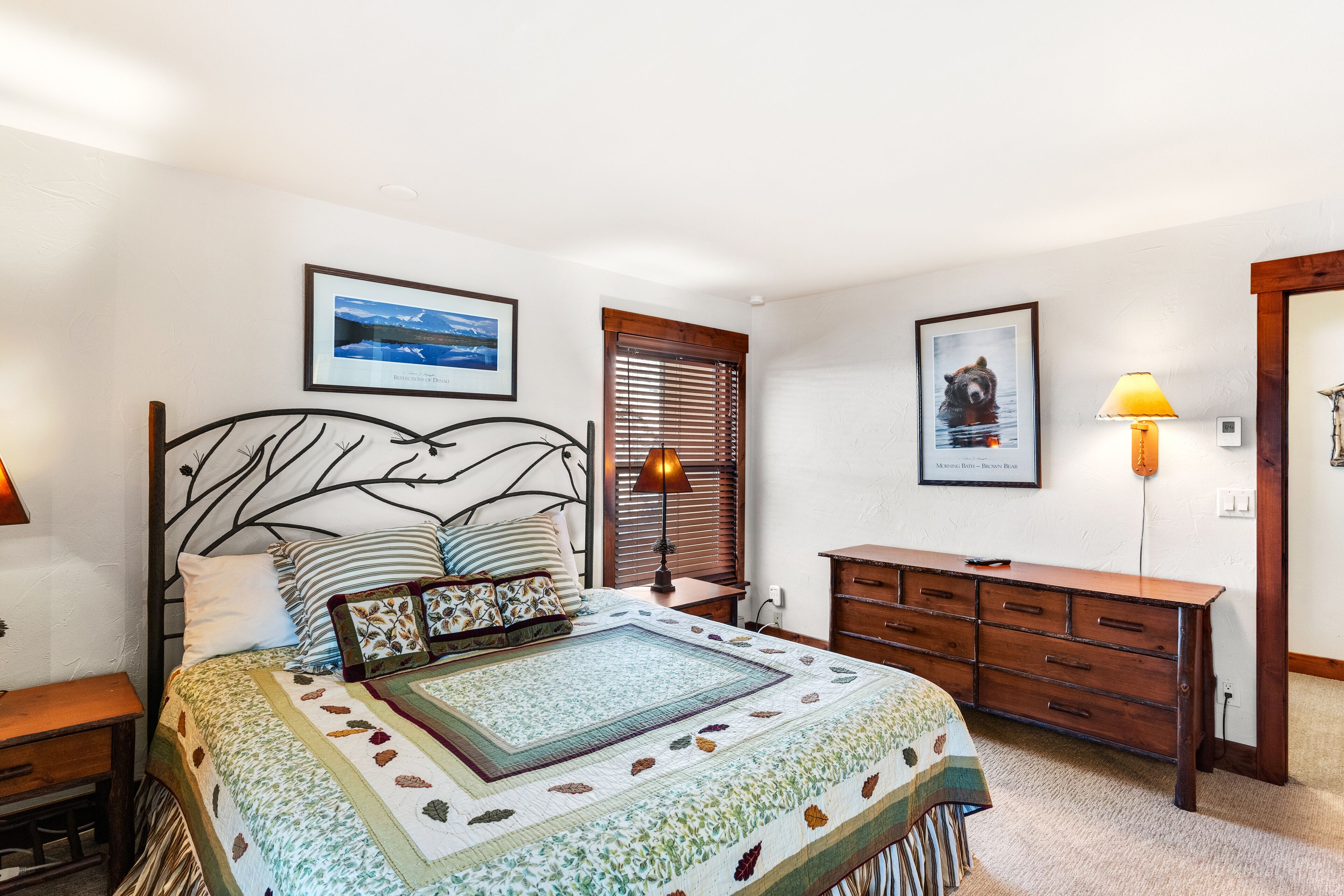 A bedroom with a bed, a dresser, a nightstand, a lamp, and two framed pictures on the wall.