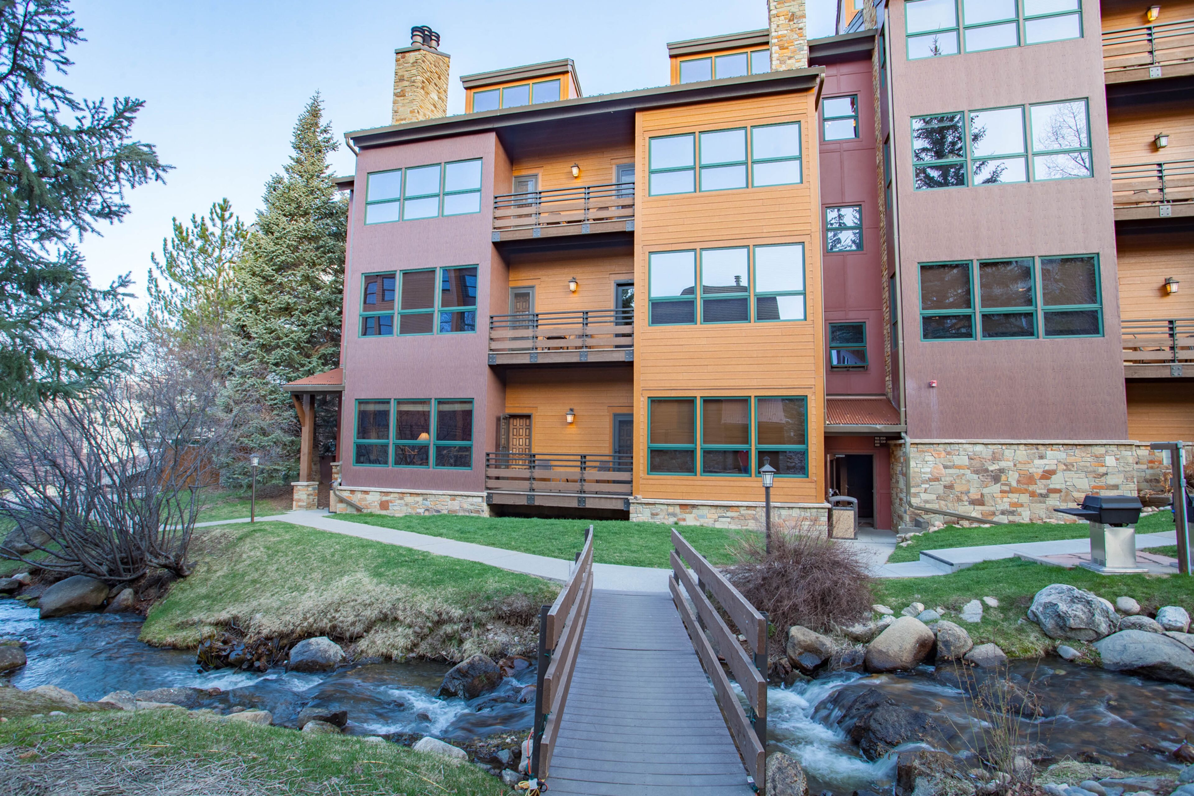 A multi-story building with balconies, a stone facade, and a wooden bridge over a stream.