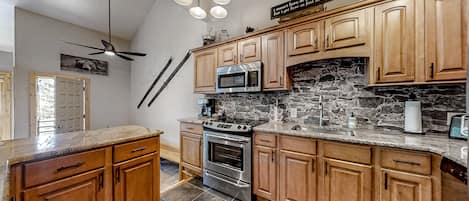 Eine Küche mit Holdekor-Schränken, einer Stein-Spritzschutzwand, einer Mikrowelle, einem Backofen und einem Deckenventilator.