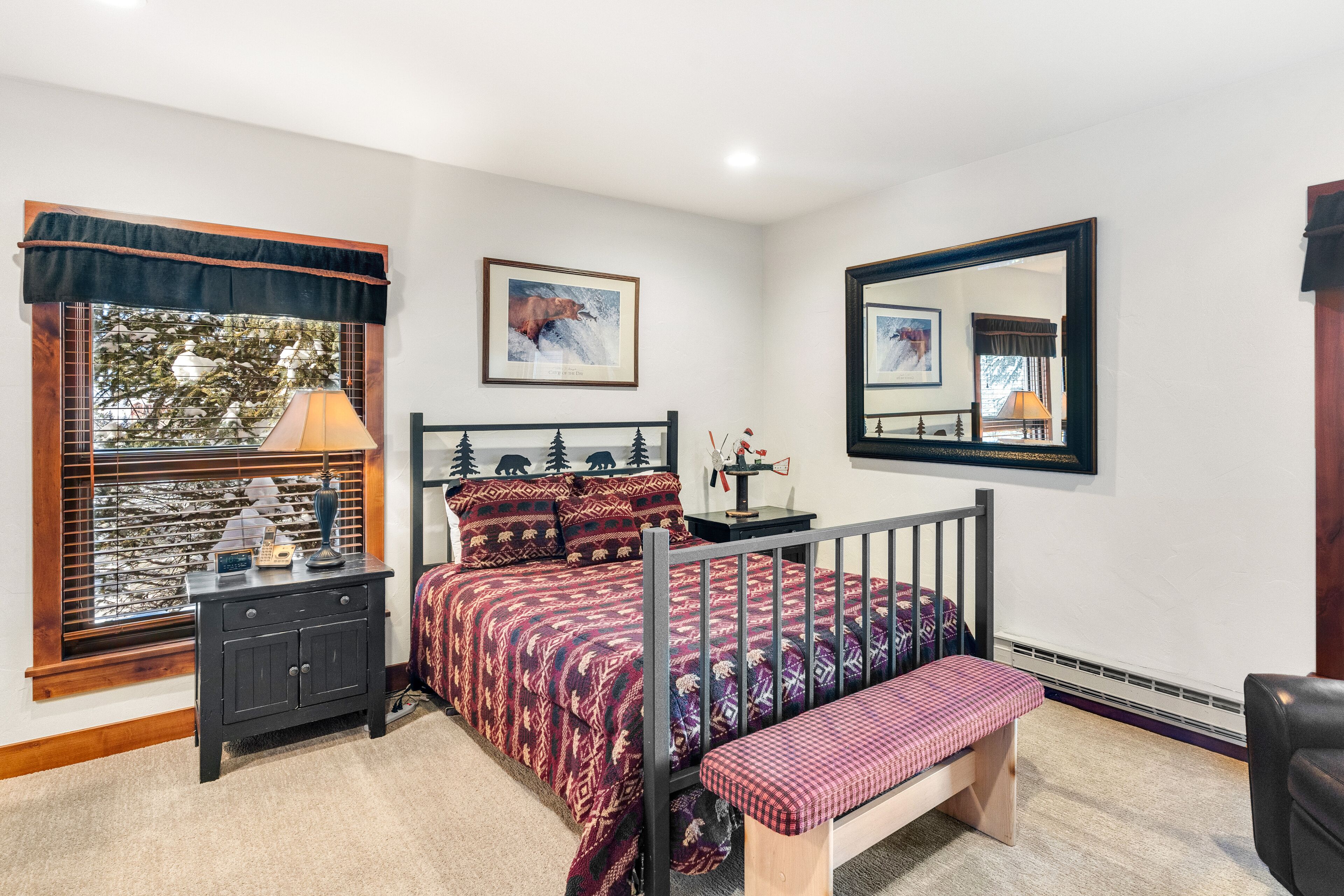 A bedroom with a bed, bedside table, lamp, and a window with blinds.