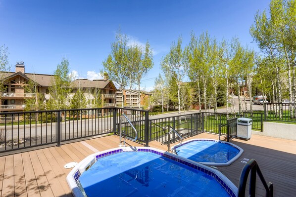 A pool area with two hot tubs, a wooden deck, and a view of surrounding buildings. - La Casa (Steamboat Springs)
