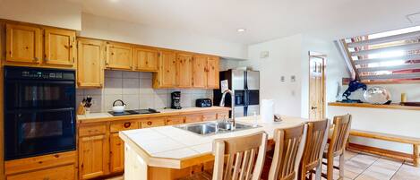 A kitchen with wooden cabinets, a black oven, a sink, and a dining area with wooden chairs.