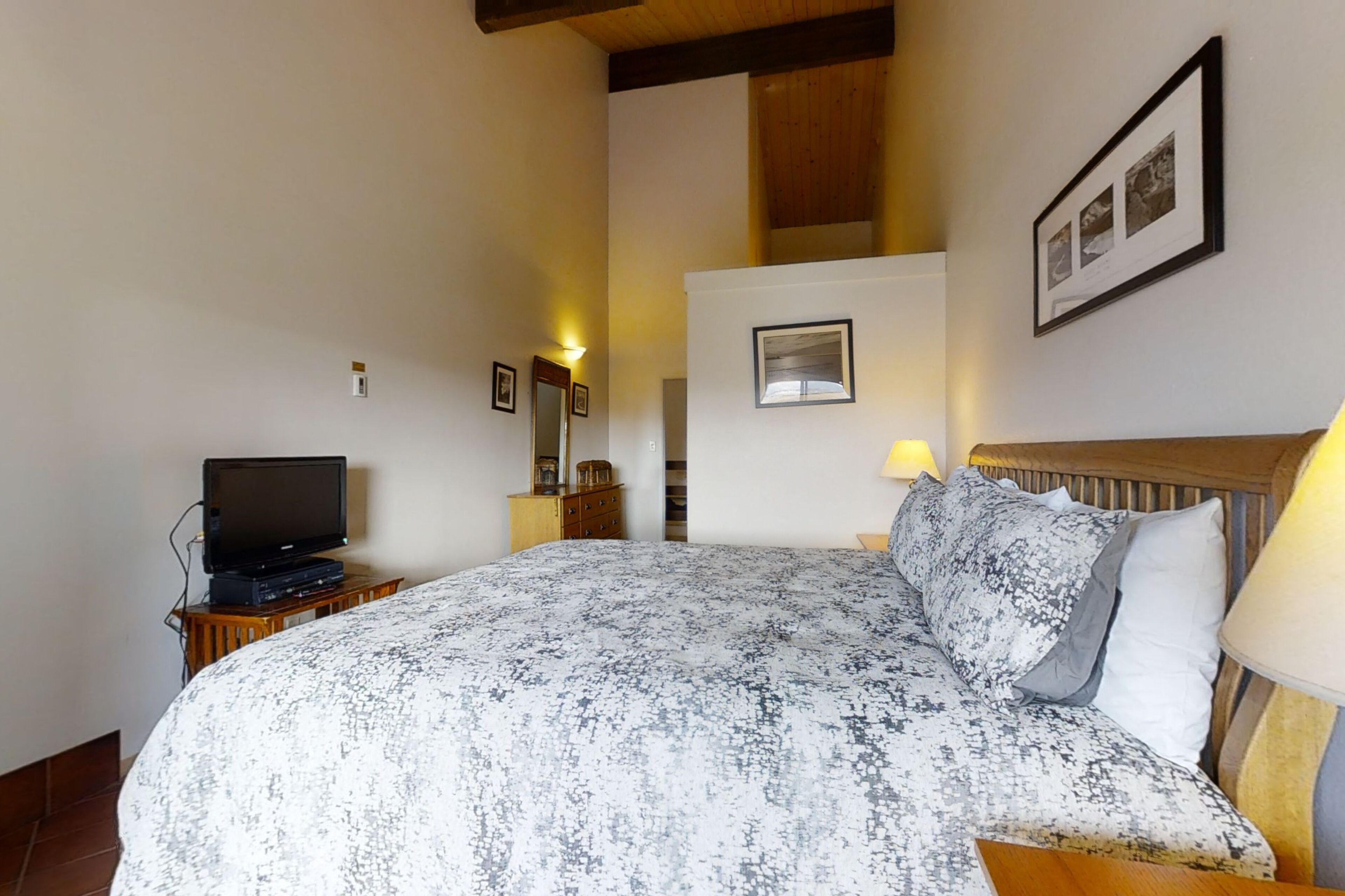 A bedroom with a bed, a television on a stand, a nightstand, and a wall-mounted picture.