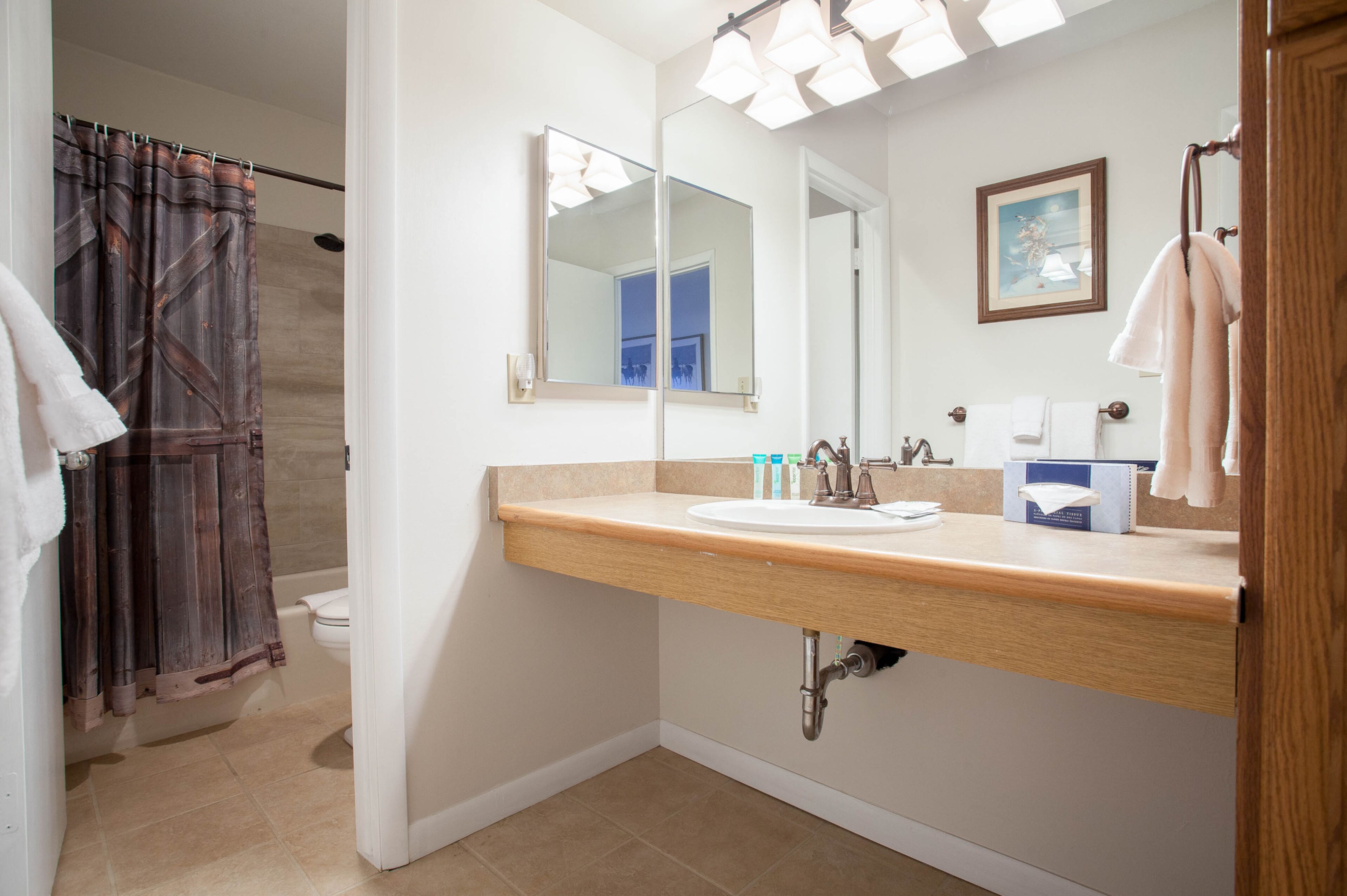 A bathroom with a wooden vanity, a large mirror, a toilet, and a shower curtain.