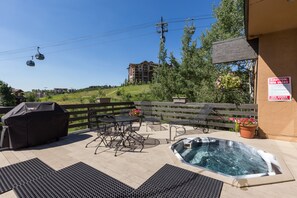 A patio area with a hot tub, outdoor seating, and a view of a ski lift and buildings in the background. - Ski Inn Condos (Steamboat Springs)