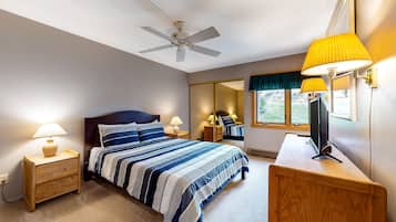 Een slaapkamer met een bed, bedlampen, een bureau met lamp, een plafondventilator en een raam met uitzicht.